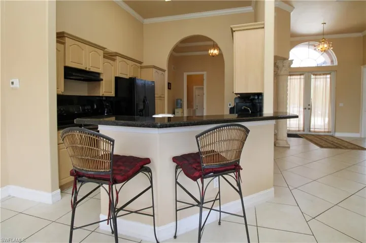 Kitchen with a breakfast bar area, dark countertops, a peninsula, under cabinet range hood, and black appliances