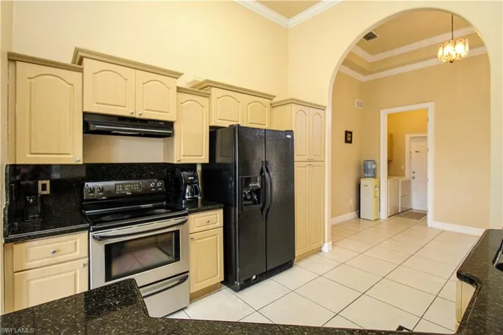 Kitchen featuring arched walkways, stainless steel electric range oven, black refrigerator with ice dispenser, and under cabinet range hood