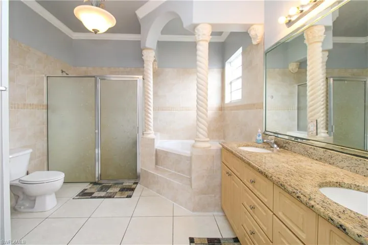 Bathroom with a garden tub, ornamental molding, a sink, and ornate columns