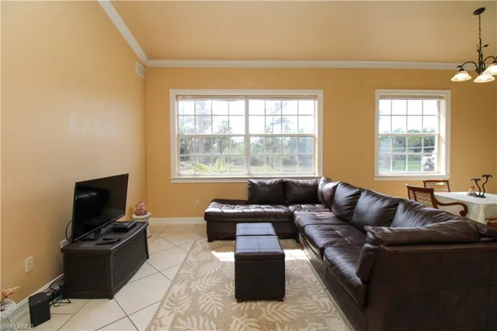 Living room with light tile patterned floors, a healthy amount of sunlight, a chandelier, and crown molding