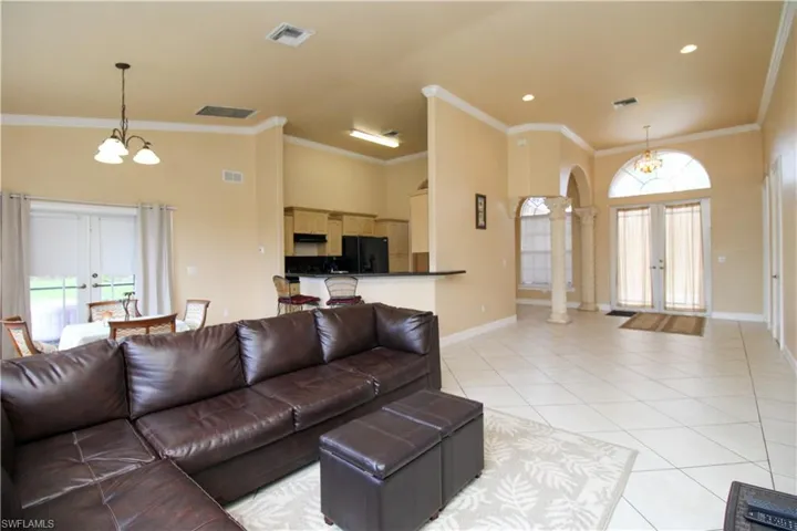 Living area with french doors, a notable chandelier, visible vents, ornamental molding, and light tile patterned flooring