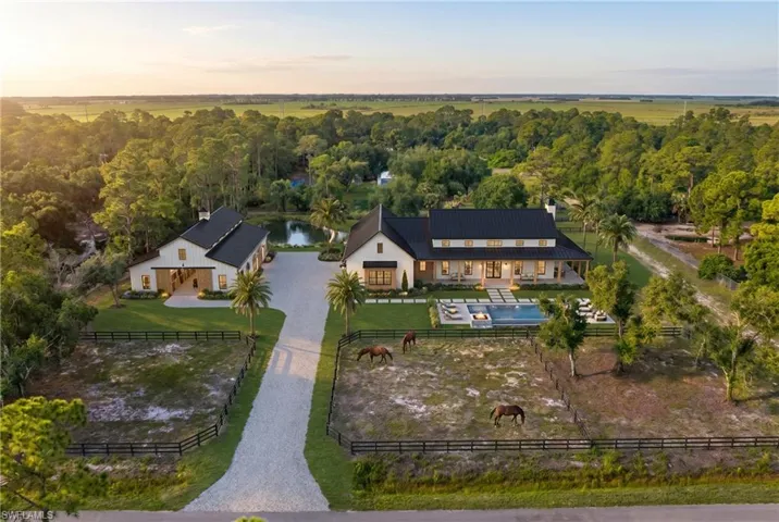Virtually Staged.  Expansive property featuring a modern farmhouse-style residence with a black metal roof, a detached barn-style structure, a large swimming pool with integrated lounge areas, a generous gravel driveway, and multiple fenced paddocks