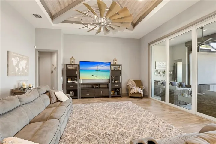 Sit back and relax while you watch TV and the outdoor activity at the same time.  Living room featuring a ceiling fan, wood finished floors, and a tray ceiling.