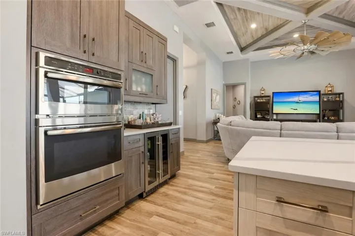 Kitchen featuring stainless steel double oven, coffered ceiling, wine cooler, beamed ceiling, and light wood-type flooring