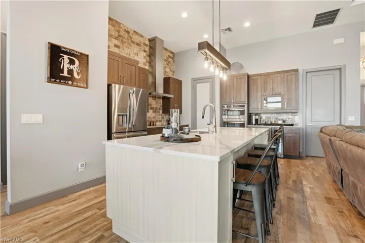 Kitchen featuring tasteful New York SOHO Brick backsplash, a kitchen breakfast bar, high end appliances with stainless steel finishes, an island with Pompei Luxury Quartz Counters with Stainless Steel sink, and light wood finished floors.