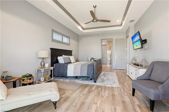 Primary Bedroom with light wood finished floors, a ceiling fan, recessed lighting, and a raised ceiling