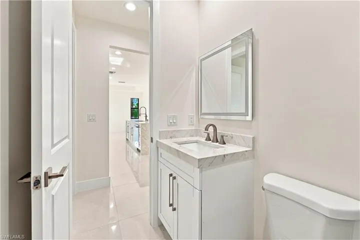 White vanity with integrated sink, stone countertop, bronze-finish faucet, and an illuminated mirror