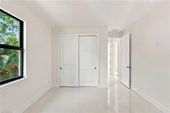 White wall paint, white trim, white sliding closet doors, white interior door, and light-toned tile flooring