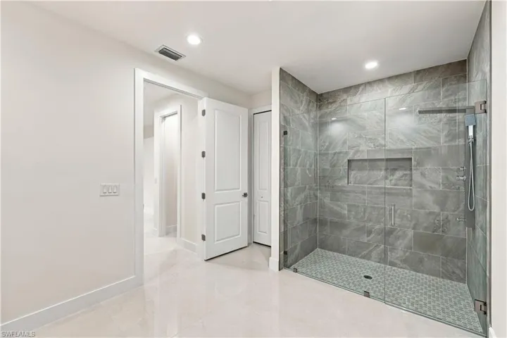 Walk-in shower with full glass enclosure, grey stone-finish tile surround, integrated shower niche, and mosaic tile flooring