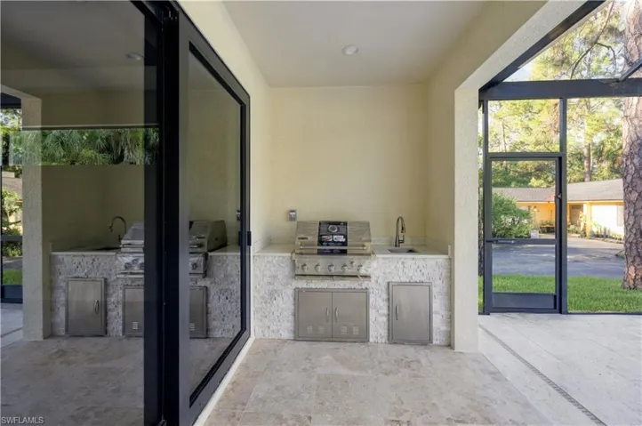 Outdoor kitchen featuring a built-in grill, sink with a gooseneck faucet, integrated storage, and stone tile surround