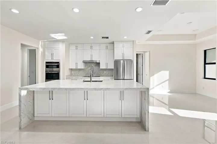 Spacious kitchen featuring an extended waterfall island, stainless steel appliances, recessed lighting, white shaker cabinetry, and light-toned tile flooring