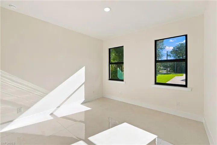 Recessed ceiling lighting, two windows with black frames, white walls, light-toned tile flooring, and white baseboards