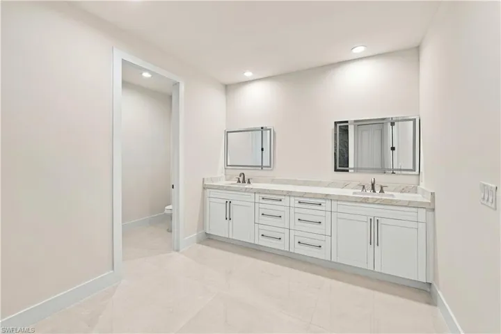 Dual vanity with white cabinetry, stone countertop, two undermount sinks with chrome fixtures, and individual mirrored medicine cabinets