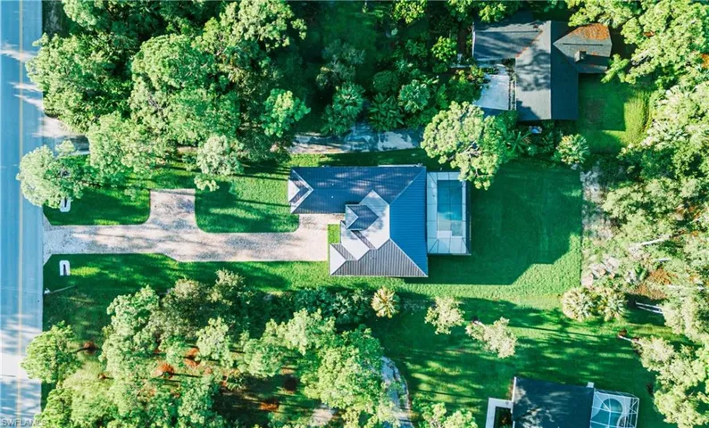 Expansive property featuring a paved circular drive, mature trees, a detached building, and an inground pool with a screen enclosure