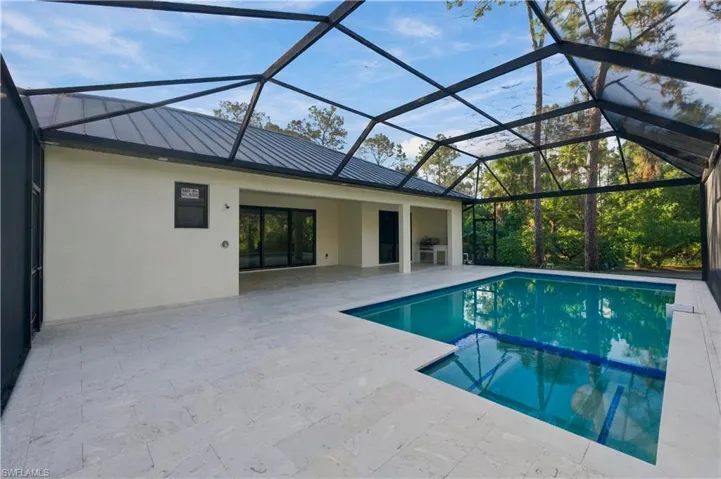 Enclosed lanai with a rectangular swimming pool, integrated spa, and expansive patio featuring light-toned pavers