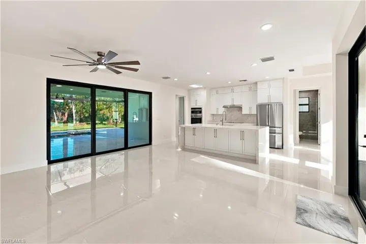 Spacious interior with large format tile flooring, modern kitchen featuring white cabinetry and stainless steel appliances, and expansive sliding glass doors