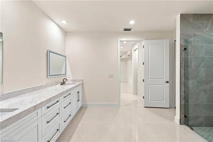 Dual vanity with a stone countertop, white shaker-style cabinetry, and matte black hardware