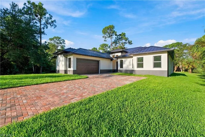 Contemporary exterior with a dark metal roof, light stucco facade, dark garage door, and brick paver driveway