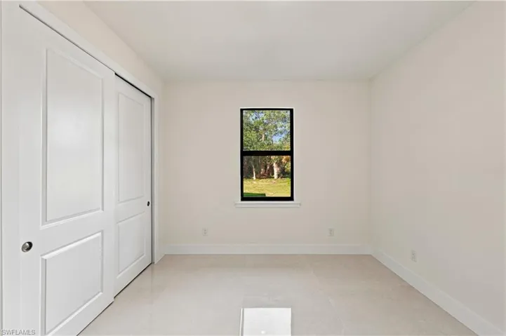 Sliding panel closet doors, single window with black trim, light-toned tile flooring, and neutral wall tones