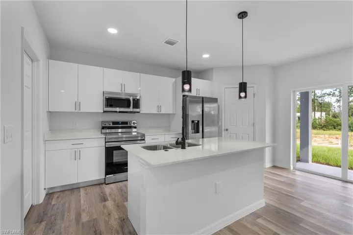 Kitchen with stainless steel appliances, white cabinets, pendant lighting, light wood-style flooring, and a center island with sink