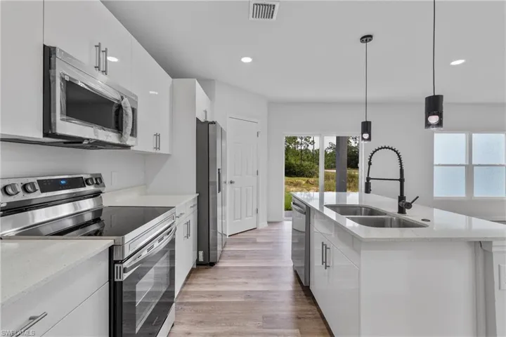 Kitchen featuring appliances with stainless steel finishes, white cabinetry, light wood-style flooring, light stone counters, and pendant lighting