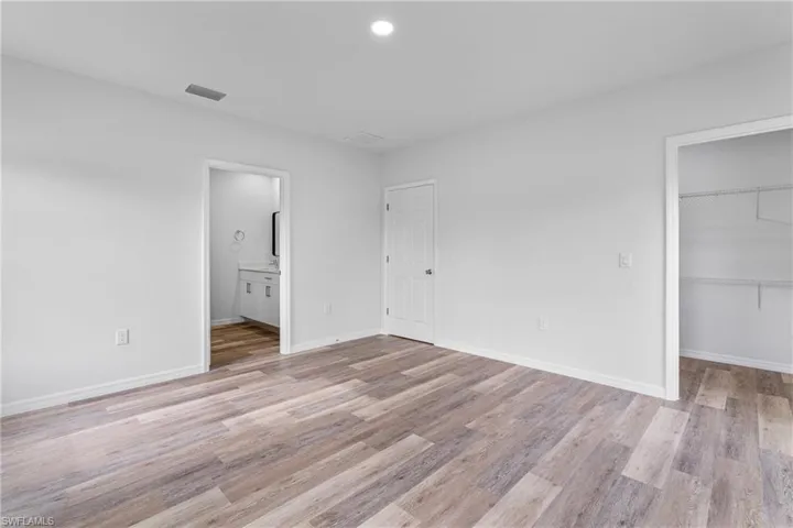 Unfurnished bedroom featuring a spacious closet, light wood-style floors, recessed lighting, and ensuite bathroom