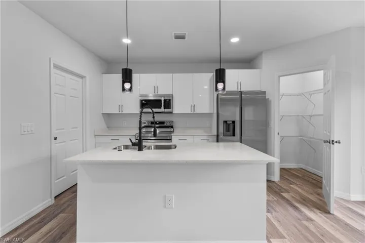 Kitchen with dark wood-style flooring, white cabinets, stainless steel appliances, pendant lighting, and a kitchen island with sink