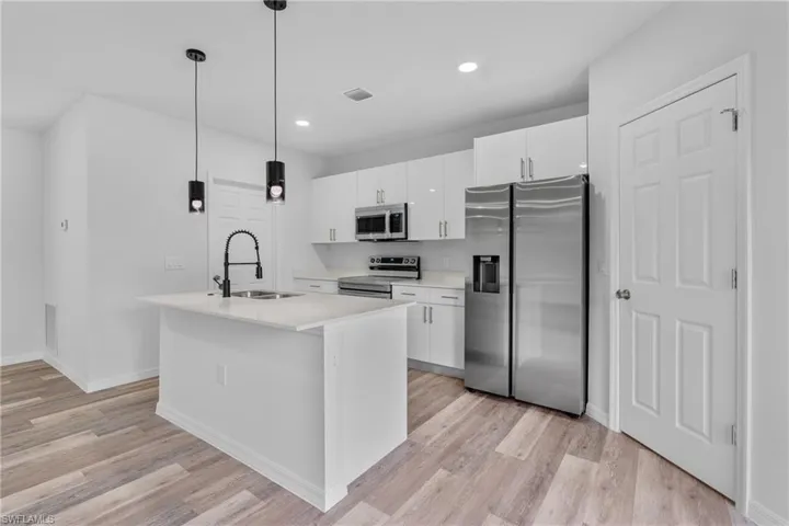 Kitchen featuring stainless steel appliances, white cabinets, a center island with sink, light wood-type flooring, and decorative light fixtures