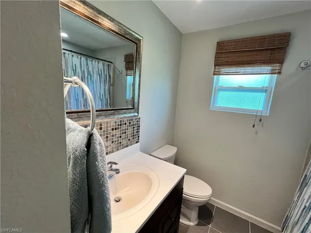 Bathroom with tile flooring, vanity with extensive cabinet space, backsplash, and toilet