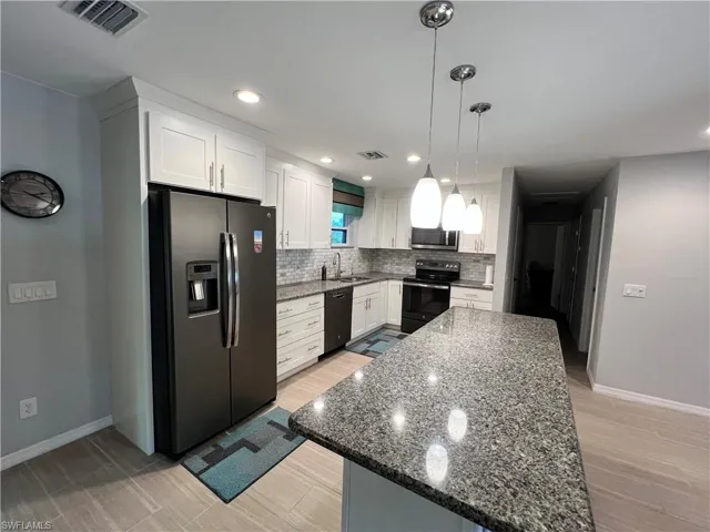 Kitchen featuring appliances with stainless steel finishes, white cabinets, tasteful backsplash, and pendant lighting