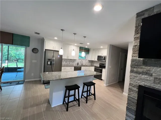 Kitchen with white cabinetry, hanging light fixtures, a kitchen island, appliances with stainless steel finishes, and tasteful backsplash