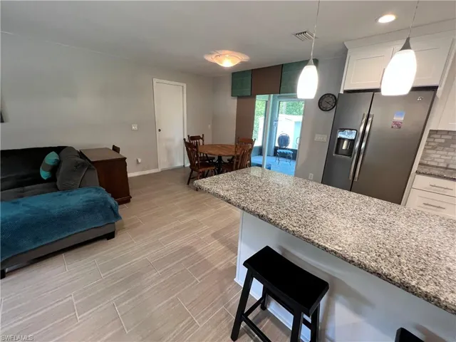 Kitchen with white cabinetry, light stone countertops, stainless steel fridge, backsplash, and pendant lighting