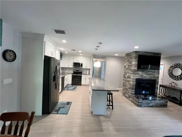 Kitchen featuring a kitchen breakfast bar, a kitchen island, stainless steel appliances, white cabinets, and pendant lighting