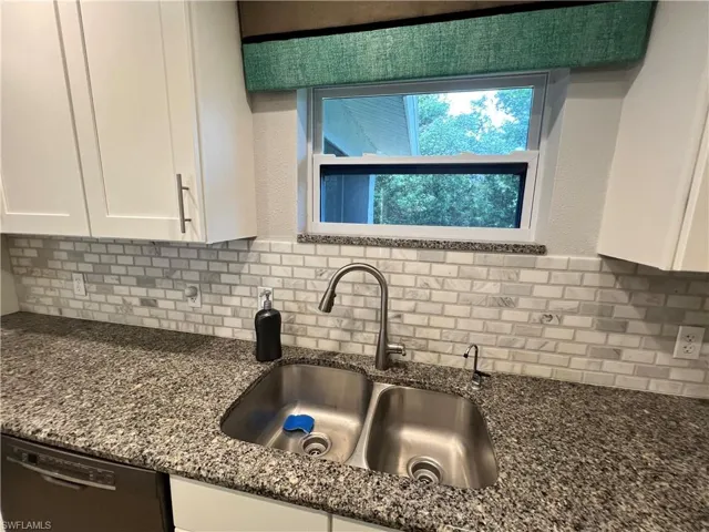 Kitchen featuring backsplash, dishwasher, stone counters, white cabinetry, and sink