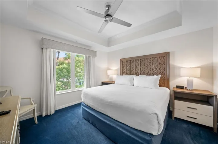 Bedroom with crown molding, a tray ceiling, ceiling fan, and dark colored carpet