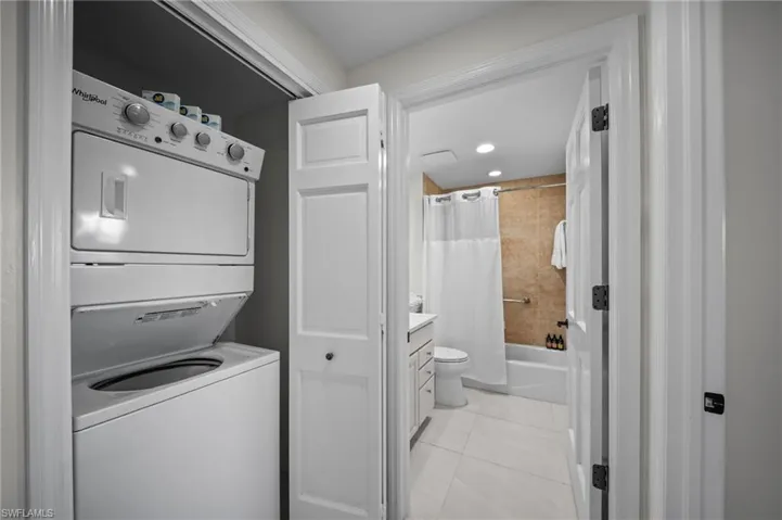 Laundry area featuring stacked washer and dryer, light tile patterned floors, and recessed lighting