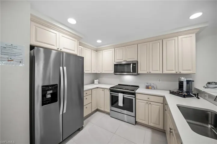 Kitchen with stainless steel appliances, cream cabinets, light tile patterned floors, and recessed lighting