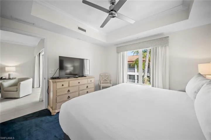 Bedroom with crown molding, a tray ceiling, dark carpet, and a ceiling fan