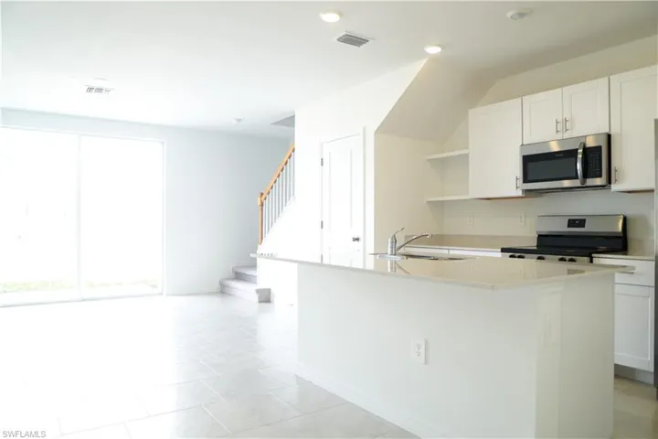 Kitchen with open shelves, white cabinets, stainless steel appliances, light stone countertops, and light tile patterned floors