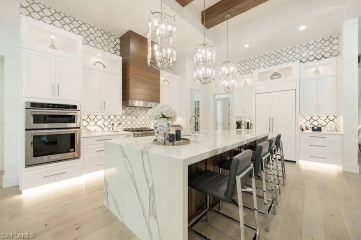 Kitchen with double oven, custom range hood, beam ceiling, decorative backsplash, and light wood finished floors