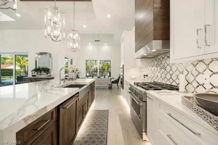 Kitchen with appliances with stainless steel finishes, a sink, wall chimney exhaust hood, a chandelier, and recessed lighting