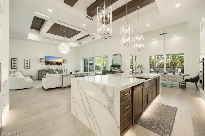 Kitchen with open floor plan, a chandelier, a towering ceiling, beam ceiling, and light wood-type flooring