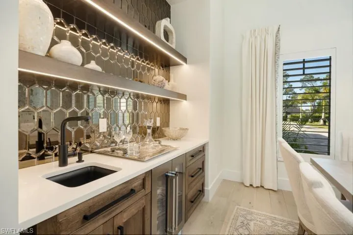 Indoor wet bar featuring wine cooler, light wood-style flooring, and baseboards
