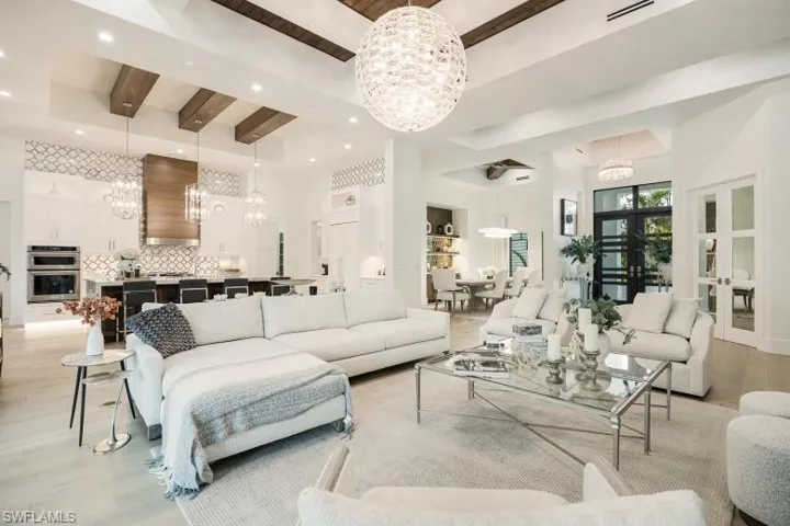 Living area with a chandelier, light wood-style flooring, beamed ceiling, recessed lighting, and a towering ceiling