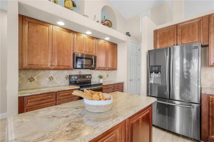 Kitchen with stainless steel appliances, light hardwood / wood-style floors, light stone countertops, backsplash, and high vaulted ceiling