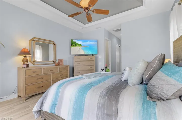 Bedroom with ceiling fan, a raised ceiling, and light wood-type flooring