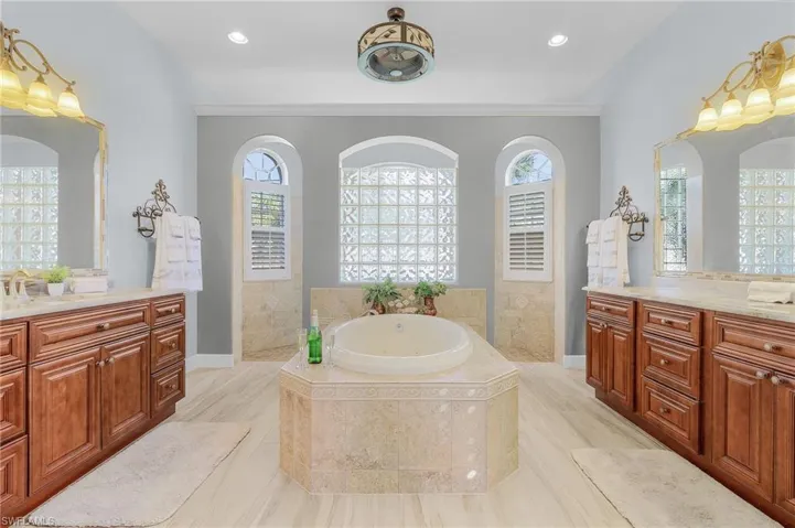 Bathroom featuring vanity, a relaxing tiled tub, a healthy amount of sunlight, and crown molding