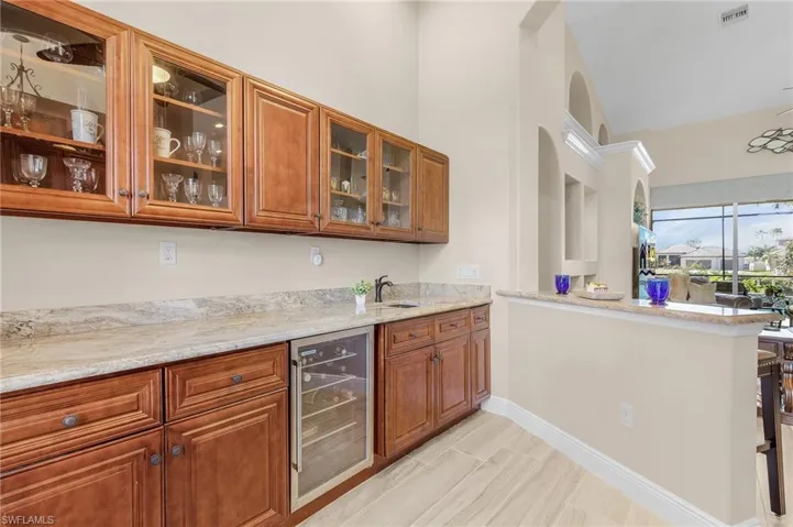 Kitchen with kitchen peninsula, vaulted ceiling, wine cooler, and light stone counters