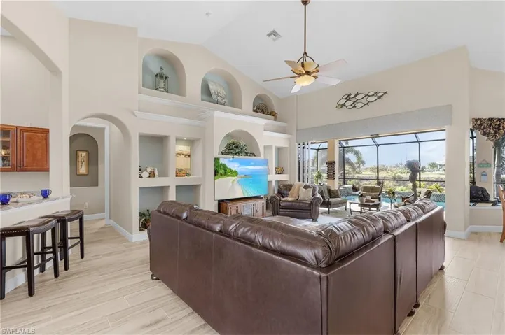 Living room featuring ceiling fan, built in shelves, light hardwood / wood-style floors, and high vaulted ceiling