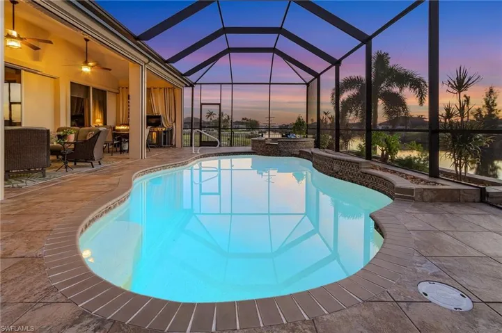 Pool at dusk featuring glass enclosure, a patio, an in ground hot tub, and ceiling fan